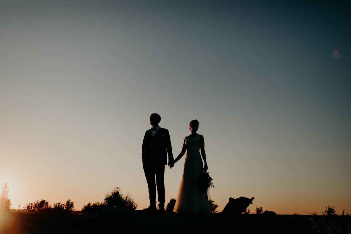 Bride and groom silhouetted against a sunset, holding hands